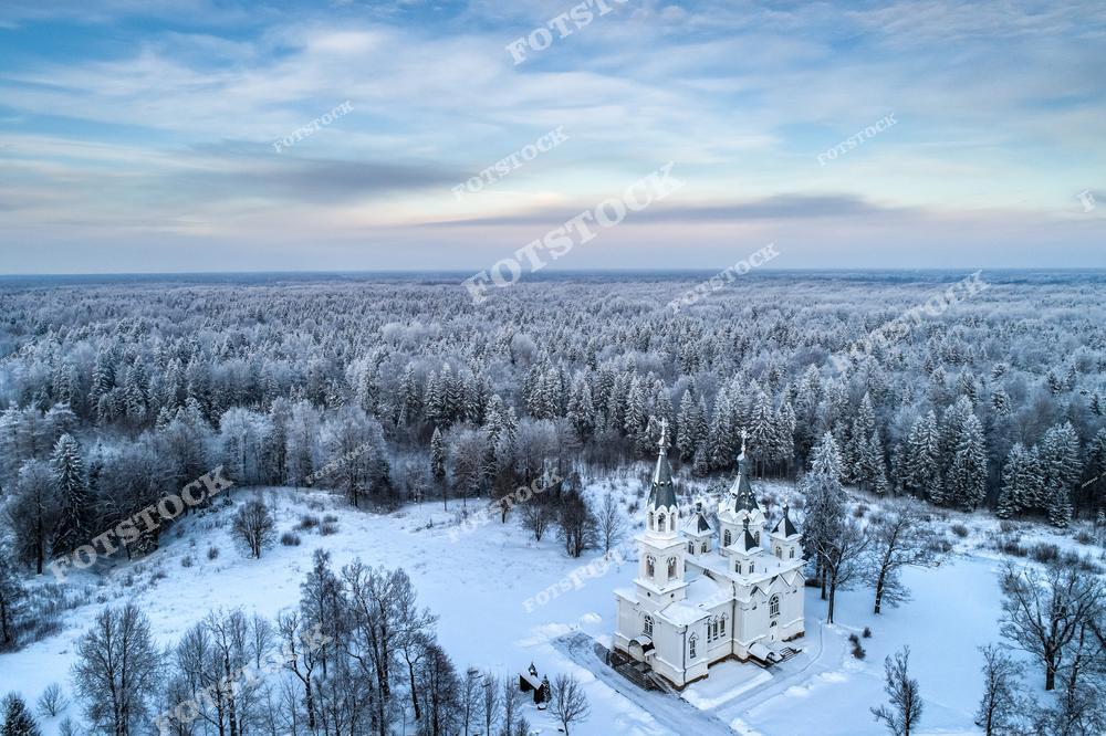Фотография православного храма в зимней тайге России. На изображении показана белокаменная Смоленская церковь, расположенная среди заснеженного северного леса недалеко от Санкт-Петербург. Фотоснимок передаёт атмосферу уединения и духовного покоя: храм окружён снегом, хвойными деревьями и тишиной северной природы. Фото отражает традиции православной архитектуры, красоту северных ландшафтов и тему путешествий по северу России. Иллюстрация может использоваться как изображение, посвящённое храмам России, зимней природе и духовному наследию.